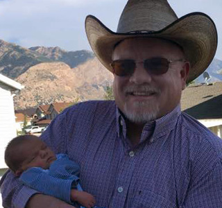 Perry Gee at home, smiling and holding an infant