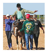 male patient riding a horse while three therapist help and walk along the horse