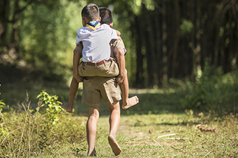 One boy scout gives another a piggy back ride down a country lane