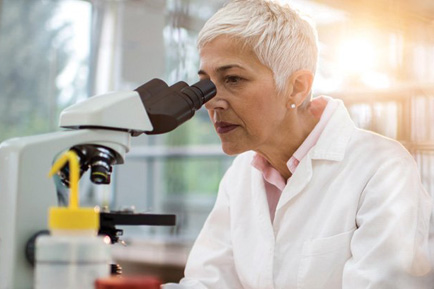 A woman in a lab setting peers into a microscope.