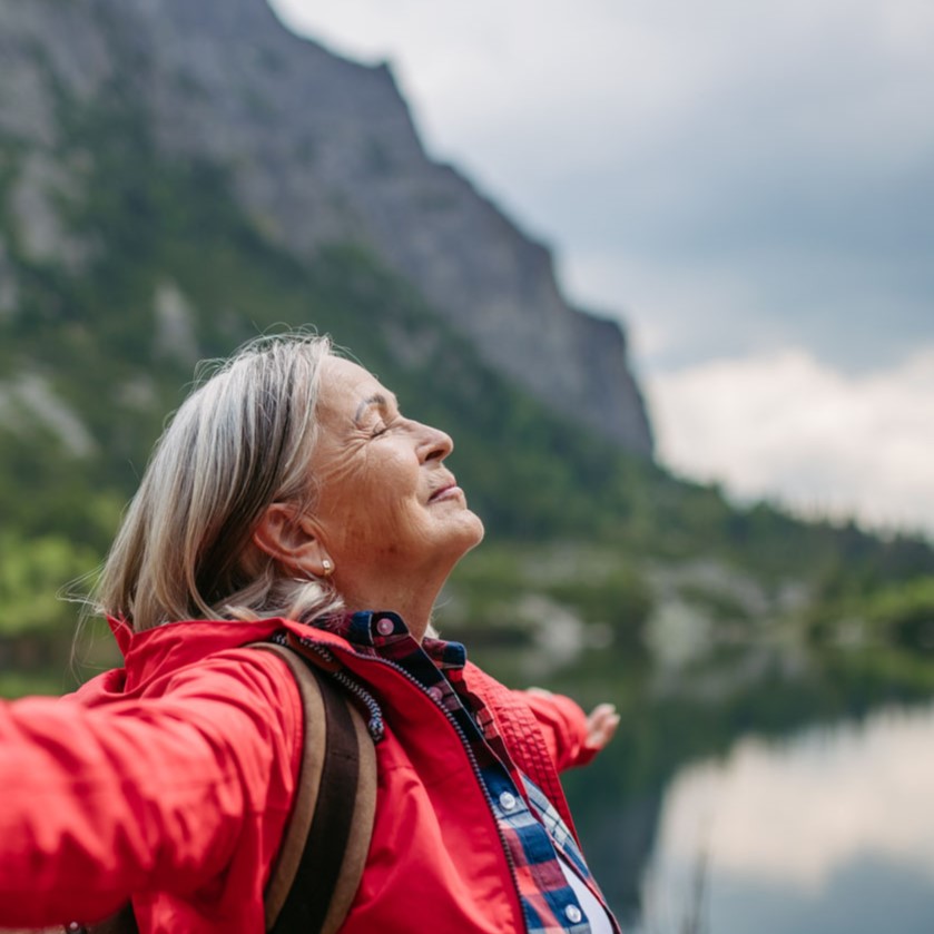 A woman opens her arms to the sky near a mountain lake